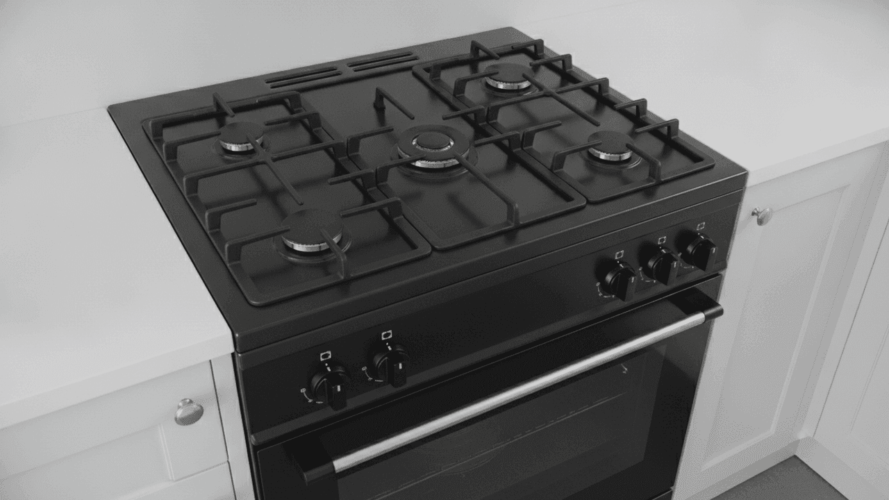 Fogão preto a gás visto do alto, com cinco queimadores apagados e grades pretas sobre a mesa, cinco botões pretos no painel e porta do forno de vidro escuro com puxador metálico, entre armários brancos